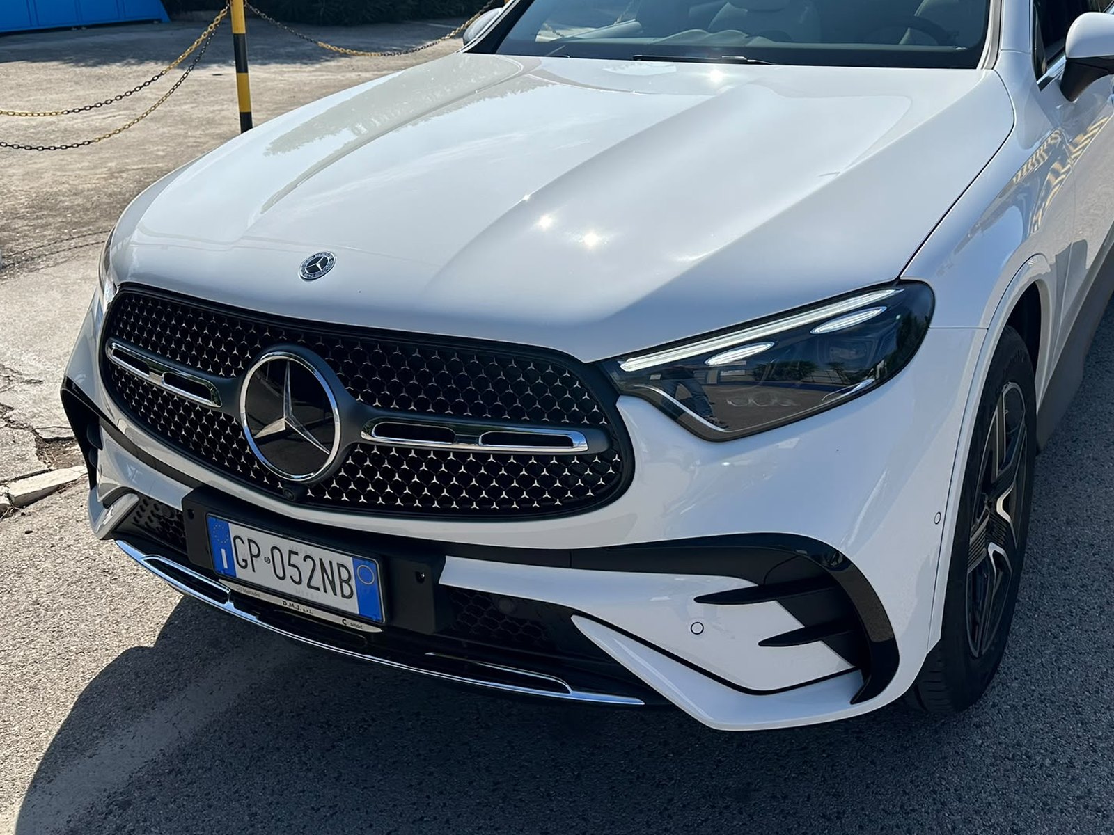 Frontale di SUV Mercedes bianco con griglia a stelle cromate e fari LED, parcheggiato su asfalto vicino a una catena