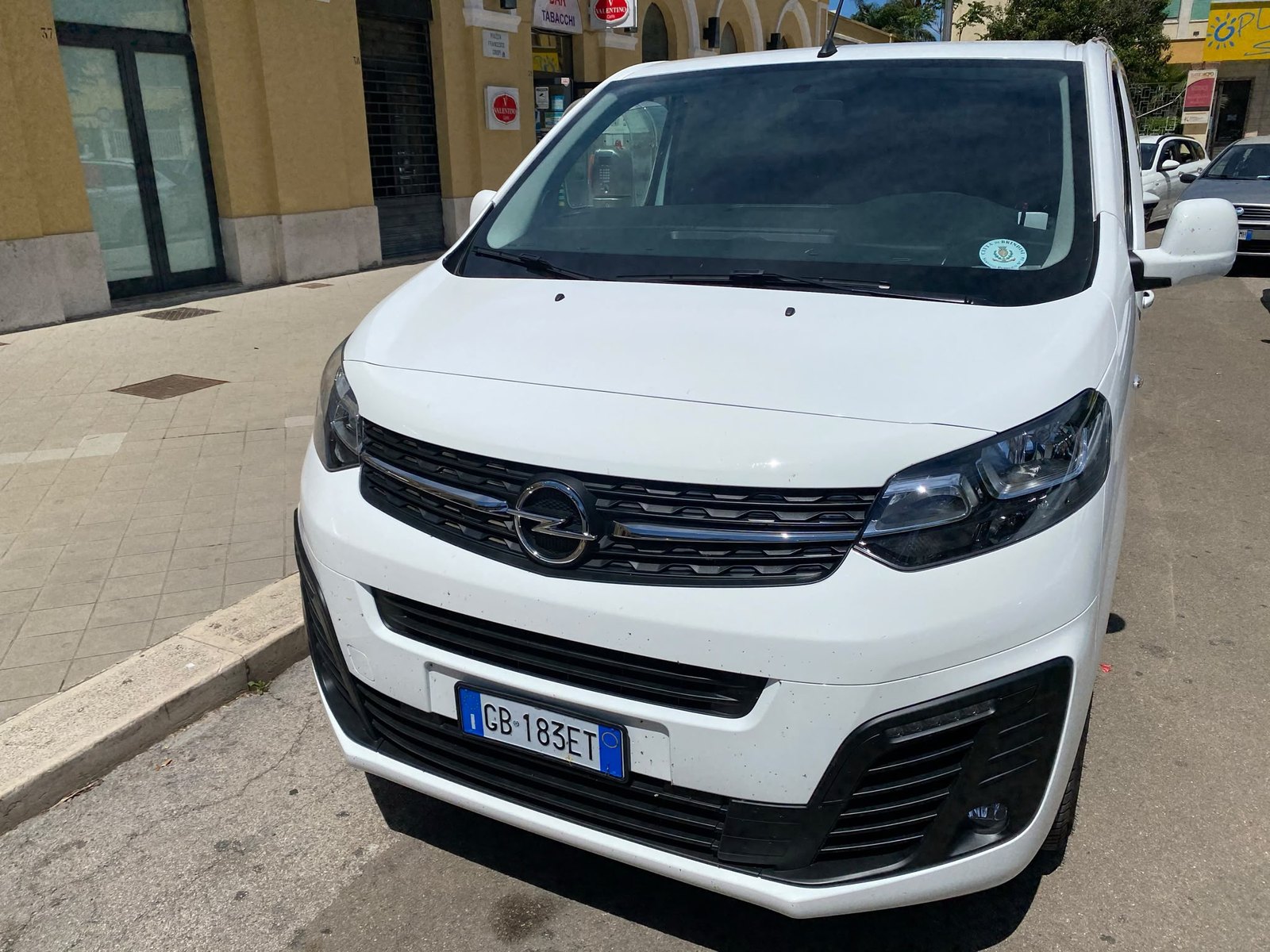 Van Opel bianco 7+1 posti di Taxi Capobianco Pietro parcheggiato lungo il marciapiede davanti a un tabacchi
